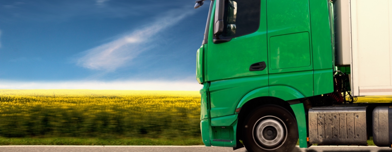 side profile of green lorry driving past field of yellow flowers