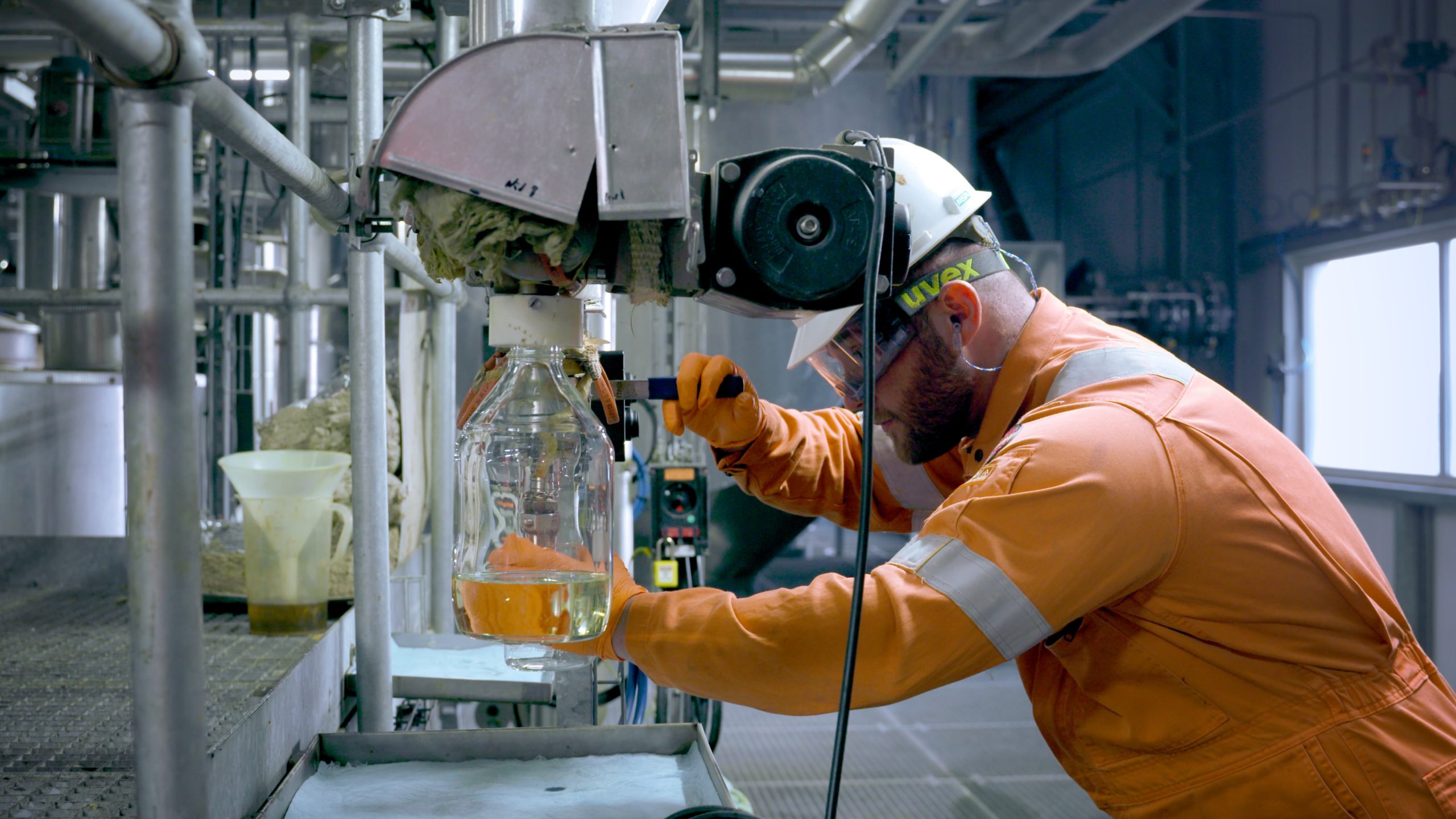 male technician with hardhat and goggles pouring out biodiesel into test beaker